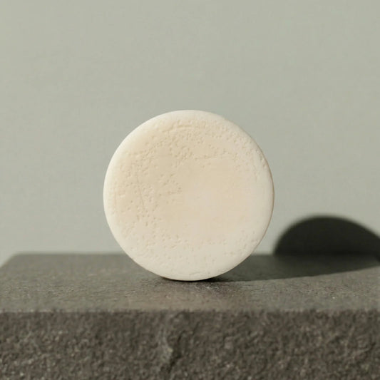 Round beige conditioner bar on a textured surface with a neutral background
