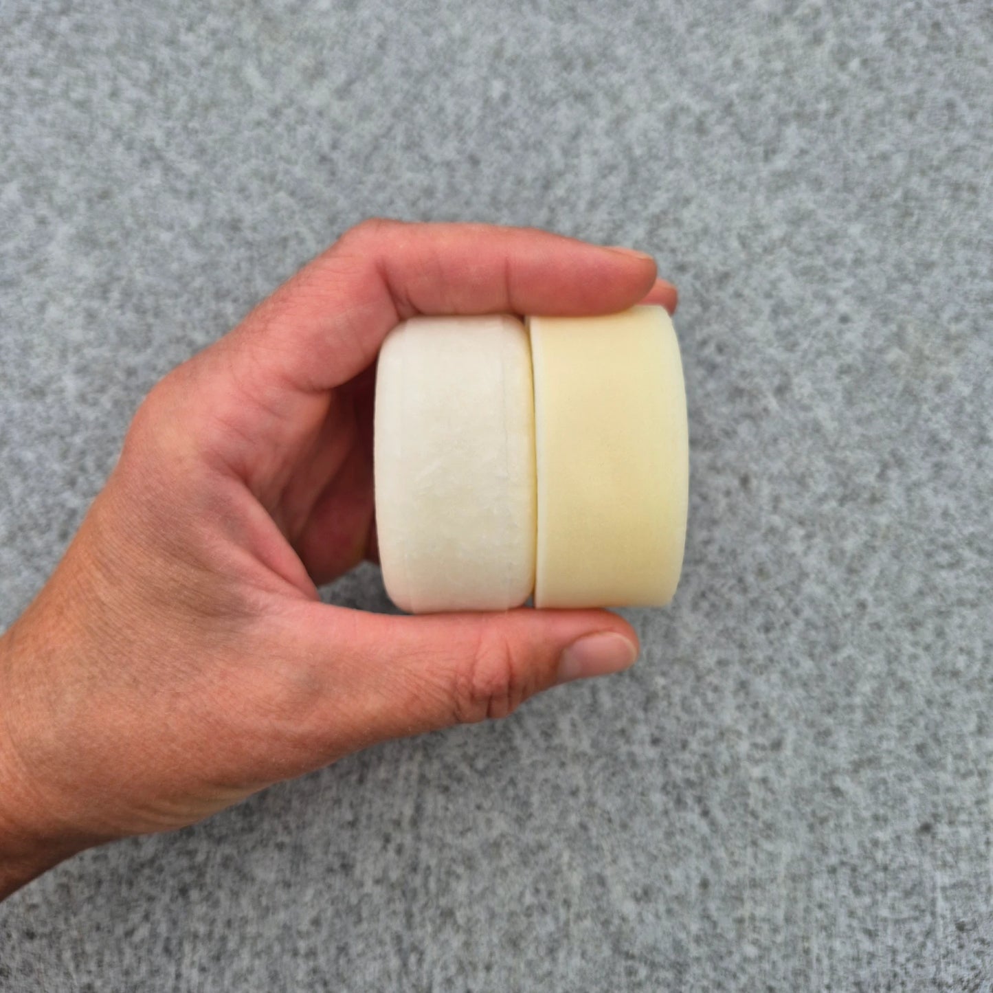 Hand holding solid hair conditioner and shampoo bars against a gray background