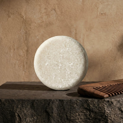 Round beard wash on a stone surface with a wooden comb against a beige wall.