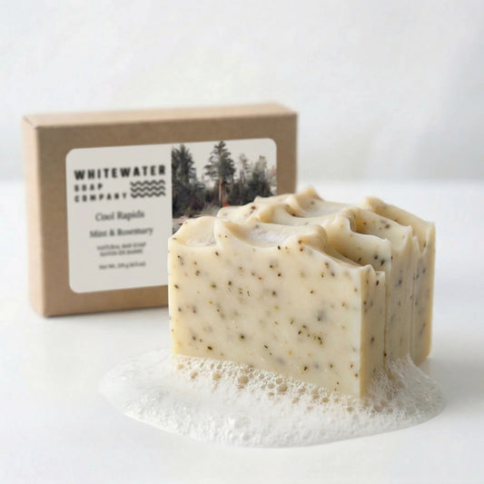 Bar of soap with visible specks and a box labeled 'Whitewater Soap Company' on a white background