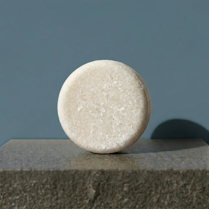 Round shampoo bar on a concrete surface with a blue background