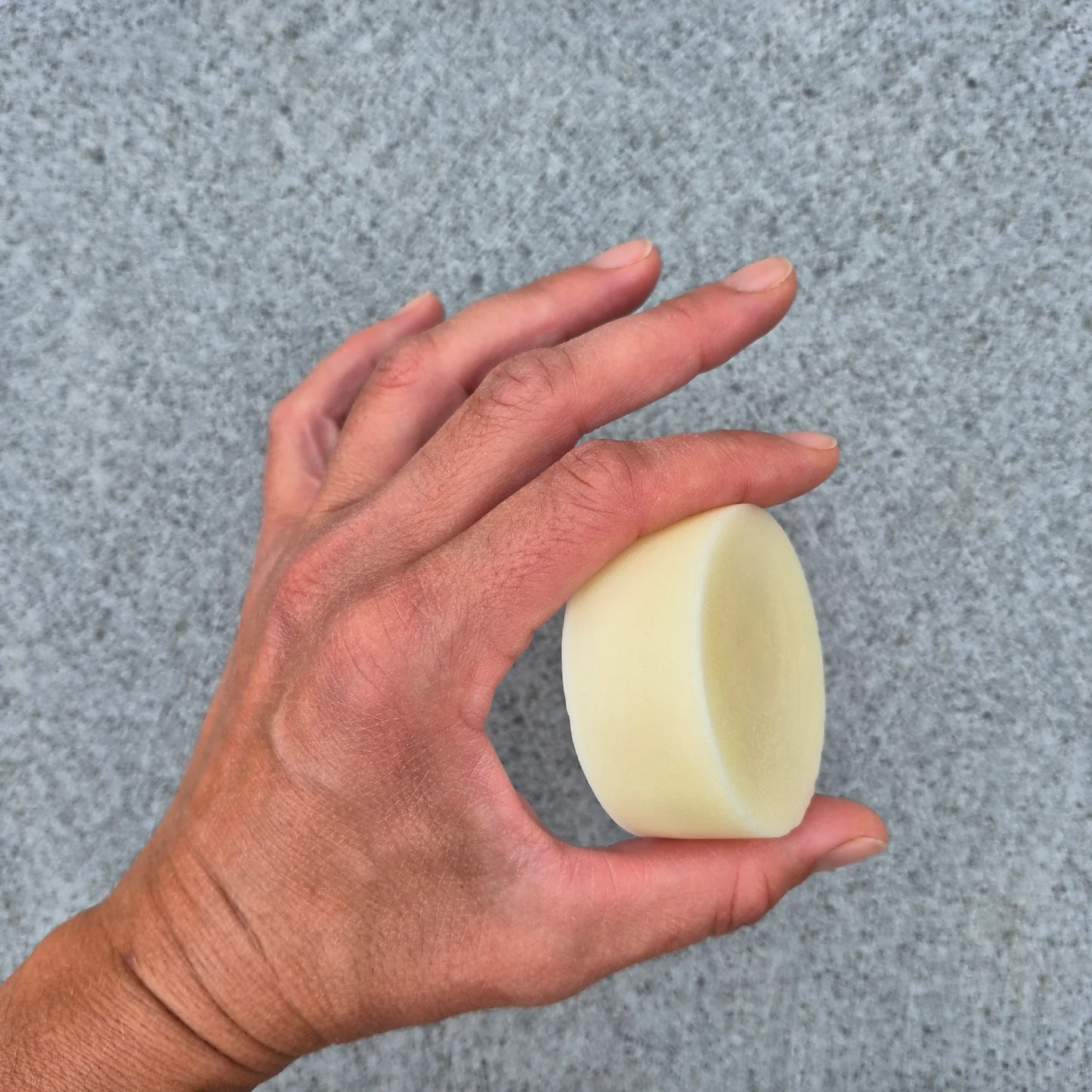 Hand holding a beige hair conditioner bar against a gray background