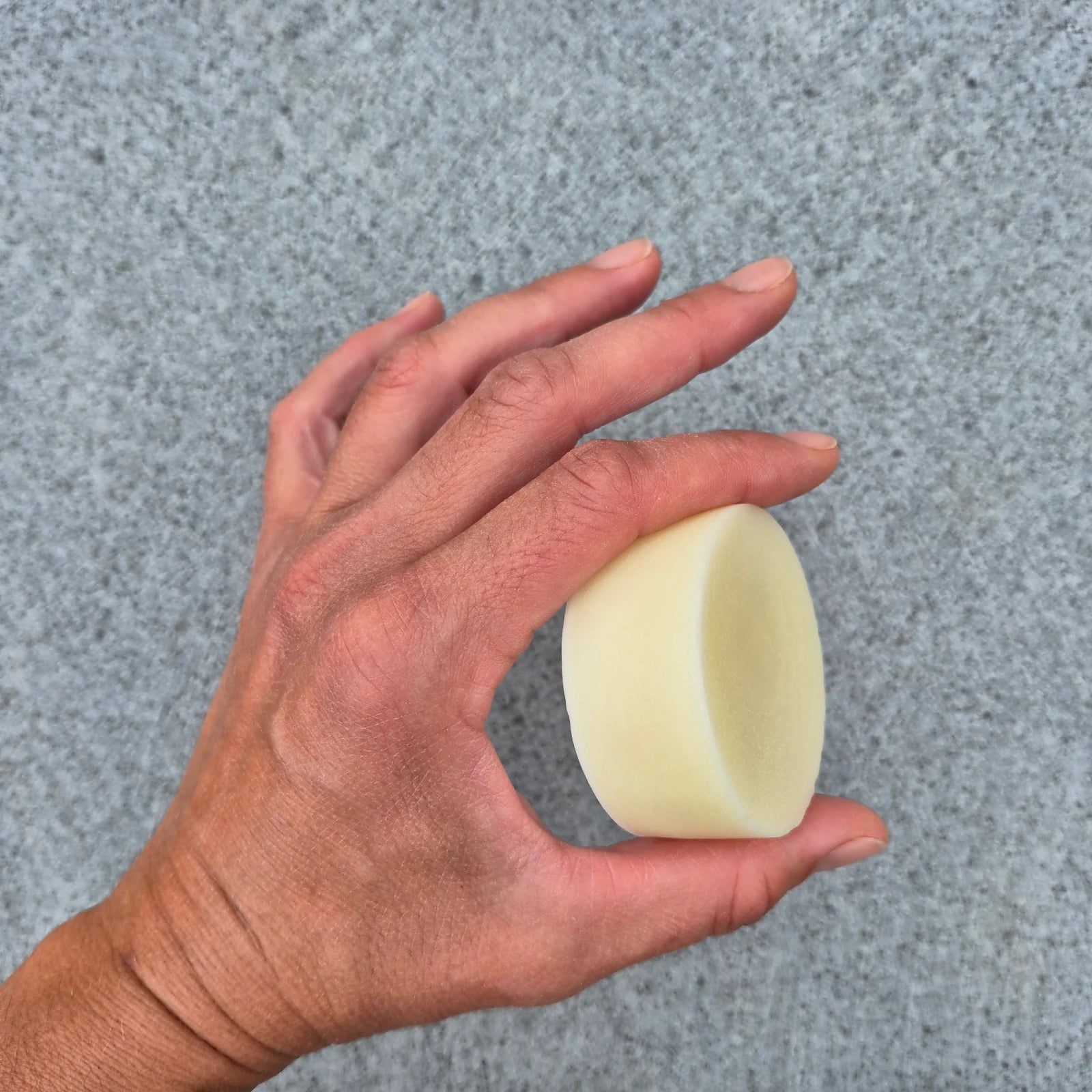 Hand holding a beige hair conditioner bar against a gray background