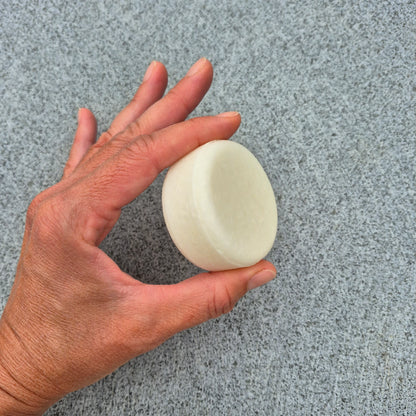 Hand holding a white shampoo bar on a gray textured background