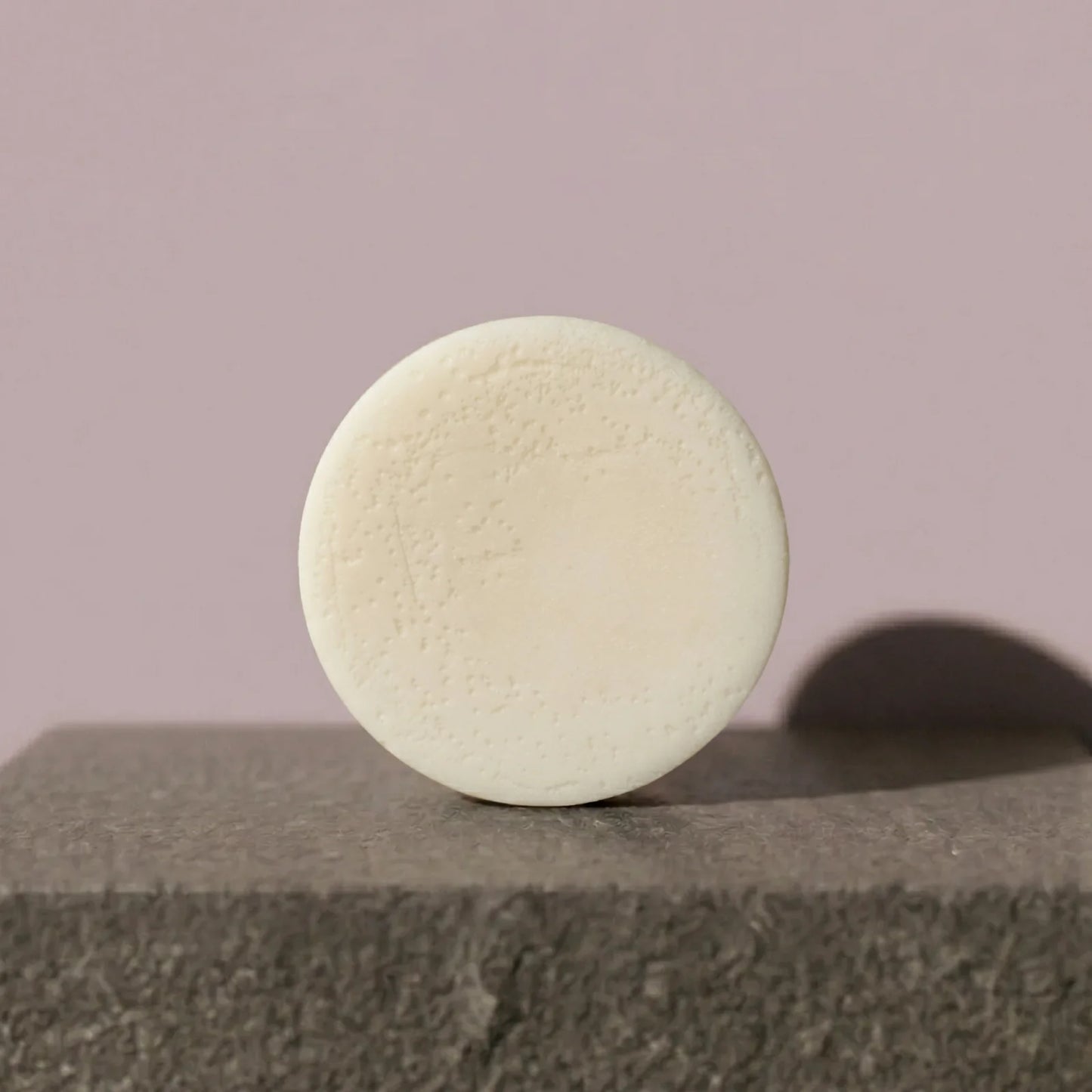 Round beige conditioner bar on a textured surface with a plain background