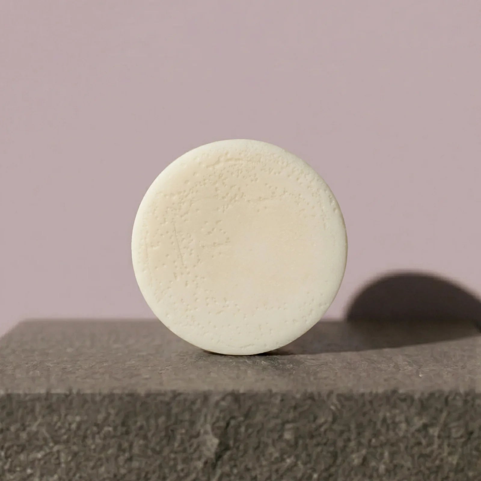 Round beige conditioner bar on a textured surface with a plain background