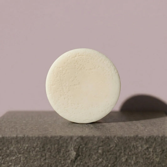 Round beige conditioner bar on a textured surface with a plain background