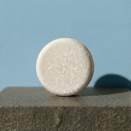 Round beige shampoo bar on a textured surface with a light blue background