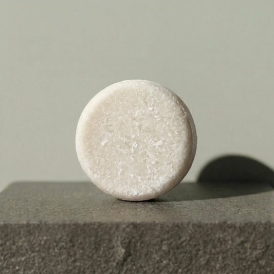 Round beige shampoo bar on a textured surface with a neutral background