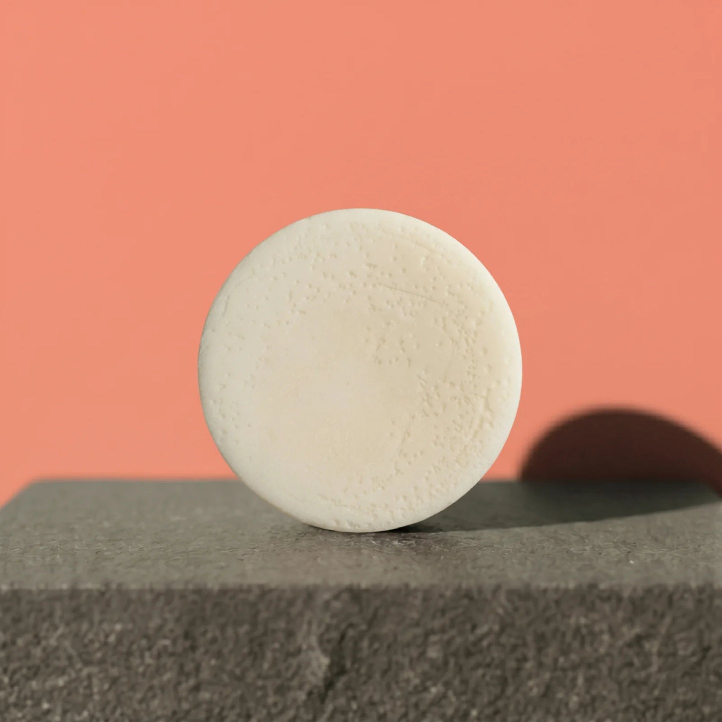 White conditioner bar on a gray surface with a pink background