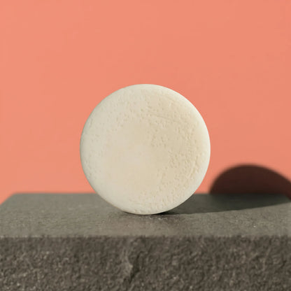 White conditioner bar on a gray surface with a pink background